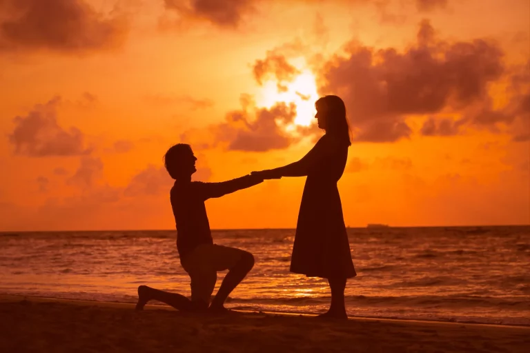 Couple sharing a romantic sunset proposal on a beach, with a stunning sunset in the background.