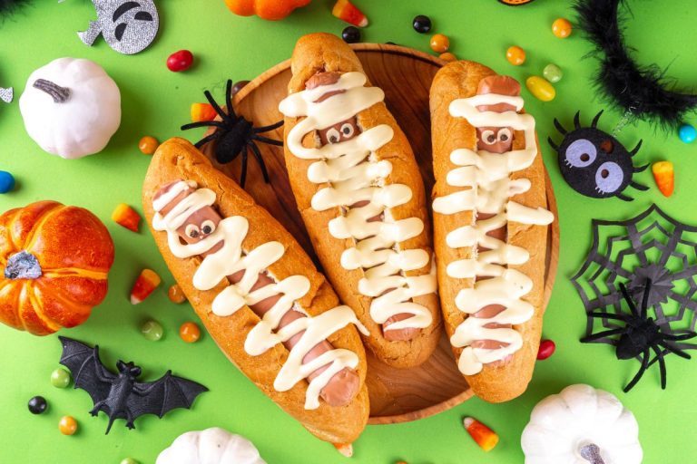 A table filled with fun and festive Halloween recipes, including mummy hot dogs, witch's brew punch, and decorated cupcakes, showcasing a vibrant Halloween celebration.