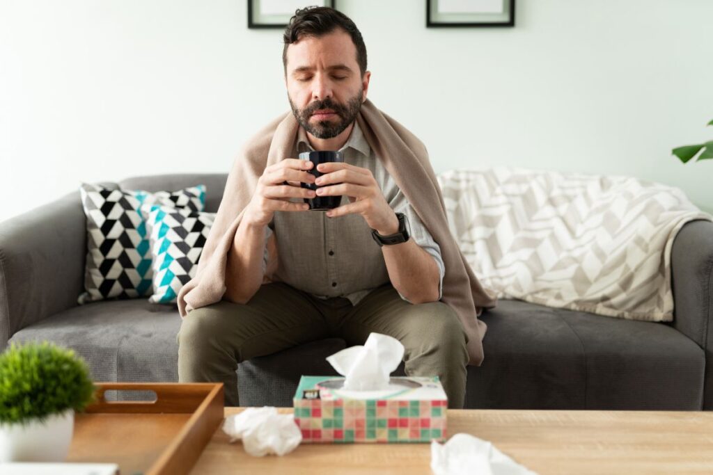 A person resting with a cup of tea, following tips to recover from a cold quickly and feel better.