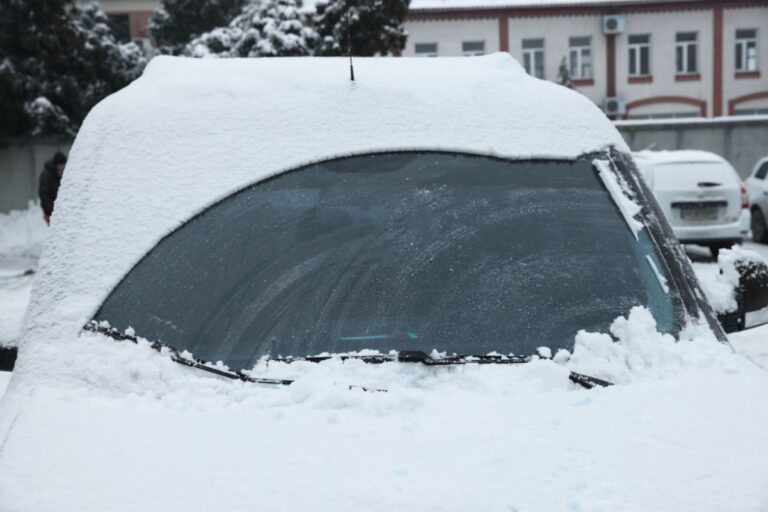 Car windshield covered in snow being cleared with an ice scraper.