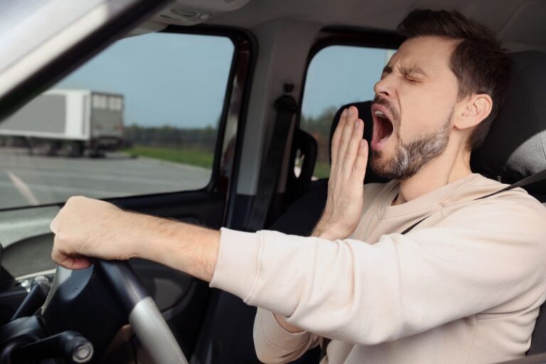 Tired driver gripping the wheel, illustrating the effects of sleep deprivation on alertness and reaction time.